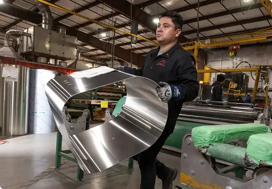 Person holding a large metal component in an industrial setting