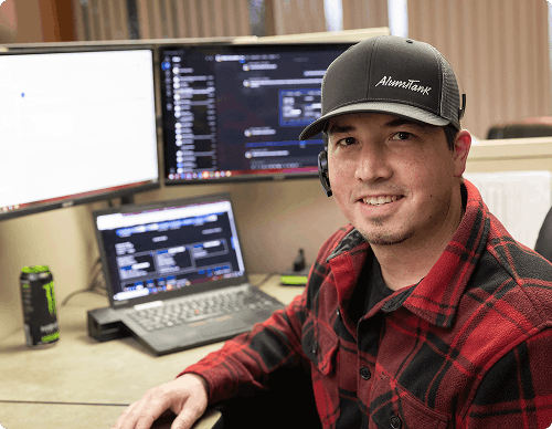 Smiling Alumitank customer service staff member at a computer workstation wearing an Alumitank cap and headset