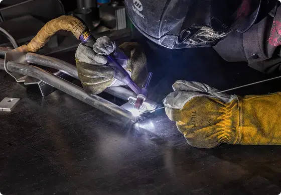 Person welding metal with protective gear in a workshop setting