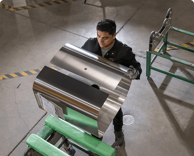 Worker handling large aluminum fuel tank components on a green cart in an industrial manufacturing facility