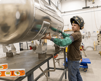 Technician inspecting and handling a large polished aluminum fuel tank in an industrial workshop