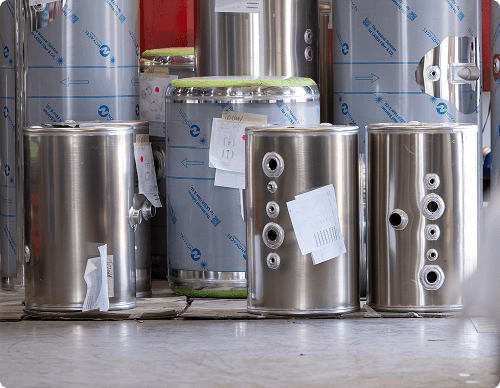 Multiple polished aluminum fuel tanks lined up in a warehouse with protective wrapping, showing various sizes with fittings