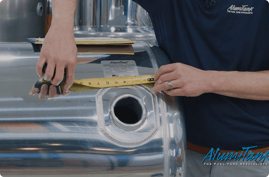 Person measuring a fuel tank with a ruler, wearing an Aluminatank shirt.