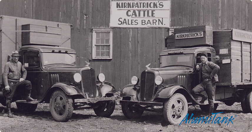 Vintage black-and-white photo of two old trucks parked in front of Kirkpatrick's Cattle Sales Barn with the Alumitank logo