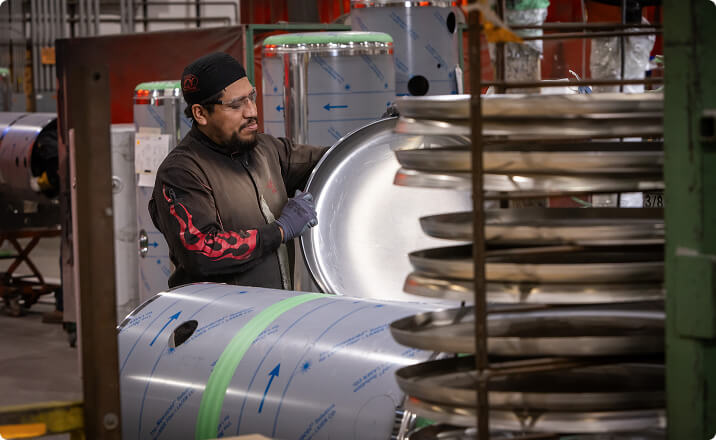 Worker handling aluminum tank components at dealerships manufacturing facility