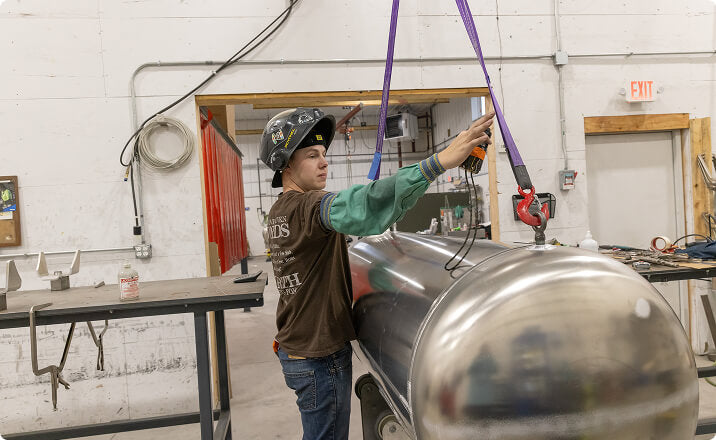 Worker lifting a large aluminum tank in a manufacturing workshop