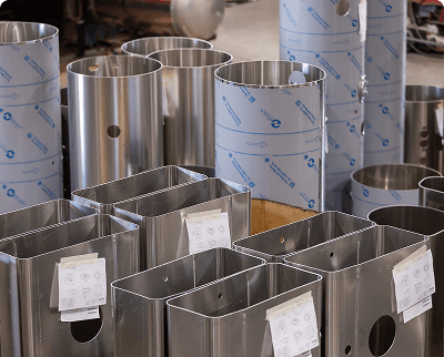Multiple aluminum fuel tank components including cylindrical bodies and rectangular parts with protective wrapping on a warehouse floor