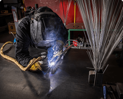 Welder in full protective gear welding metal on a workshop floor with bright sparks flying
