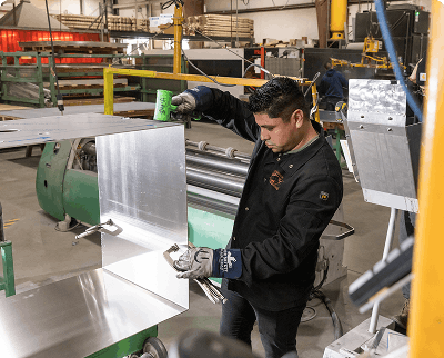 Worker handling aluminum sheet metal on a fabrication machine in a manufacturing factory
