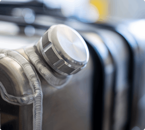 Close-up of a polished aluminum fuel tank valve cap fitting on a row of finished fuel tanks