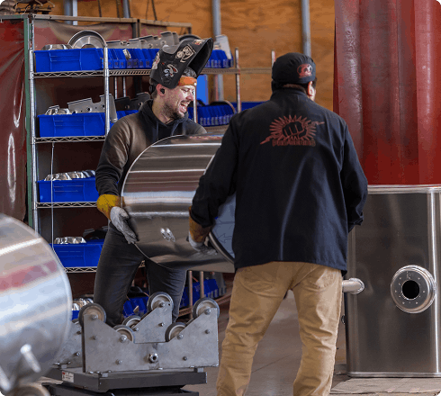 Two Alumitank workers collaborating to move and position an aluminum fuel tank component in a manufacturing workshop