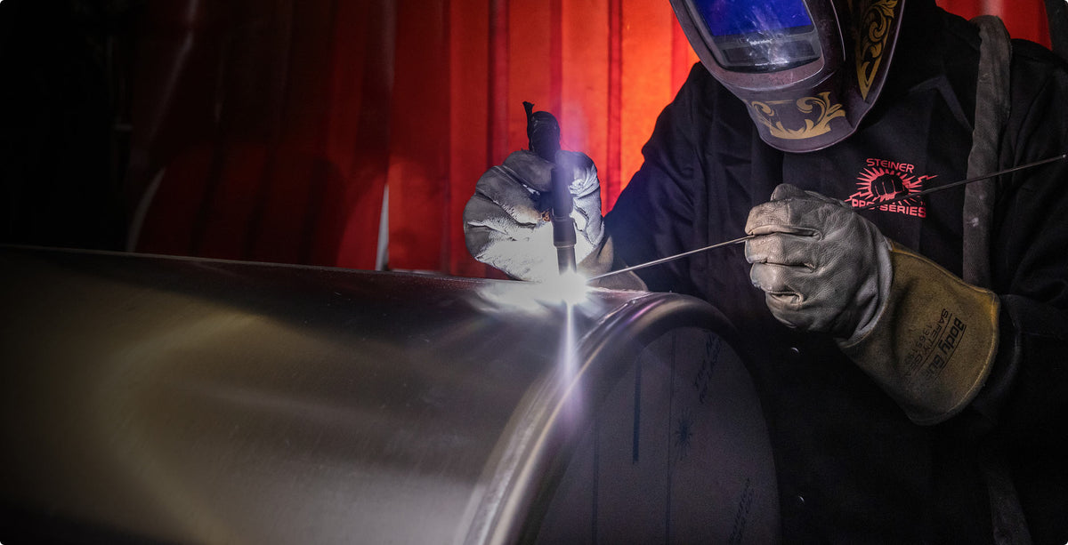 Person welding a large metal pipe with a red curtain in the background