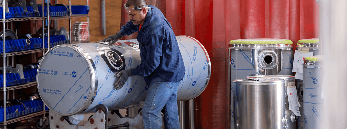 Person working with large cylindrical metal tanks in a storage area.