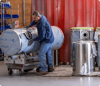 Person handling large cylindrical metal tanks in a warehouse setting