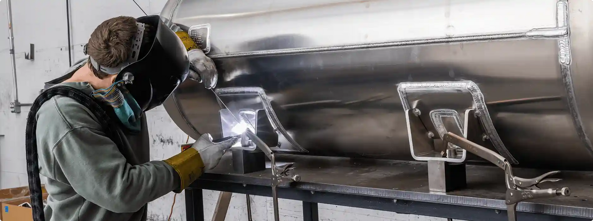 Person welding a large metal tank in a workshop setting