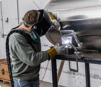 Person welding a large metal tank in an industrial setting