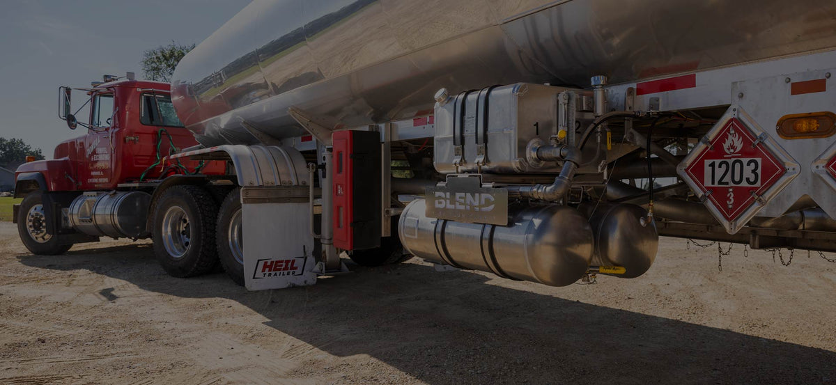 Large red fuel tanker truck with a Heil trailer and polished aluminum fuel tank parked on a dirt road